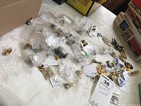 Lot of costume jewelry pieces scattered on a table with clear plastic bags and paper tags visible.