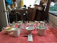 Full spread of various creamers on pink quilted cloth showing different materials, colors, and designs including ceramic and glass.