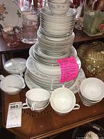 Stacked Crestwood Heritage china plates, cups, saucers, and serving pieces on a wooden table with a price note attached.