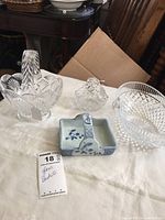 Four baskets displayed on white cloth, three clear glass baskets and one porcelain basket with blue floral decoration.