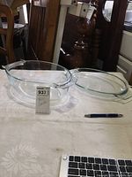Clear glass oval roaster dish and matching lid placed next to a pen and keyboard for scale.