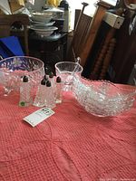 Etched floral footed bowl, press cut gravy boat, four side serving dishes, and six salt and pepper shakers arranged on a pink textured cloth.