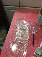 Six clear glass luncheon plates and one clear glass handled mug with grape design, placed on a red quilted surface. Pen visible for scale.