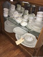 Full view of the china set displayed inside a cabinet showing the plates, cups, creamers, and sugar bowls stacked neatly.