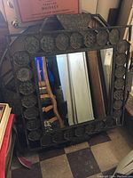 Full front view of the large square mirror showing the metal frame with multiple octagonal and rectangular patterned elements and the reflective mirror surface in the center.