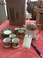 Full view of tea set on table, showing teapot, six tea cups, four saucers, and MaxSold tag.