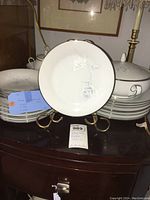 Stack of white porcelain dishes including dinner plates and lidded soup bowls, with an embossed rose floral design in relief.