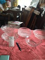 Five glass bowls of various designs on a pink cloth, with a pen for scale.