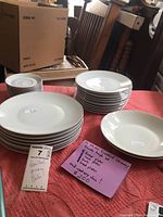 Set of porcelain plates and bowls stacked on a table with a pink cloth, alongside a card stating 'Rosenthal Germany Plates' and the lot number 7.