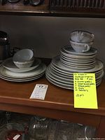 Photo showing the stacked Sheffield Imperial Gold china plates, cups, and saucers arranged on a wooden shelf.
