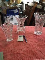 Four clear glass vases on a pink textured cloth with a pen for scale and an auction lot tag