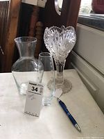 Three clear vases displayed on a white cloth with a blue pen for size reference, including the decanter-shaped vase, small etched dot vase, and the stemmed tulip vase with a decorative pattern.
