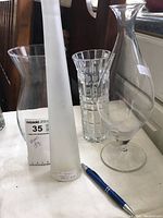 Four vases on a white surface near a window, showing different styles; frosted, geometric cut, bulbous, and regular clear glass