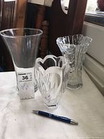Set of three clear glass vases on a table with a pen for scale.