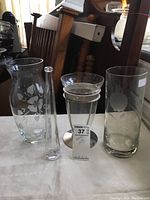 Four vases on a table with varying shapes and decorative elements including etched flowers and metal highlights.