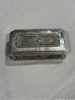 Front top angle view of the ornate cast plated antique dresser box showing the decorative raised panel on lid and side details.