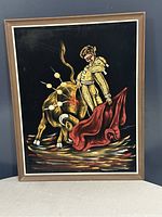 Front view of framed vintage oil painting depicting a matador facing a bull with a red cape on black background.