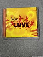 Front cover of The Beatles 'Love' CD showing yellow and orange background with silhouettes and text