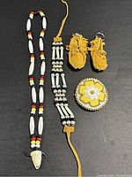 Five handmade vintage pieces displayed on a dark surface including necklace, bracelet, keychains, and brooch