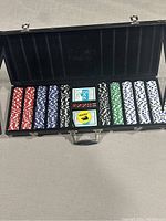 Open black poker chip case showing stacks of colored poker chips and two decks of cards inside.