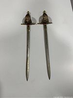 Top view of both swords laid parallel showing blades and ornate hilts with enamel decorations.