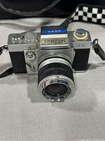 Front view of Topcon RS camera with Re.Auto-Topcor 55mm f/2.8 lens attached on gray surface