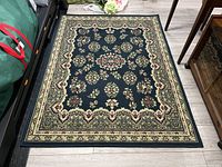Rectangular low pile olefin area rug with floral motifs and dark background photographed on light wood flooring.
