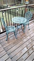 Full view of the cast aluminum bistro set showing table with two chairs on wood deck outside.