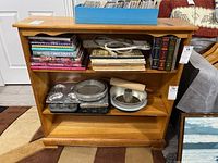 Front view of the wooden bookcase, showing books and kitchen items on shelves, scratches visible on bottom shelf
