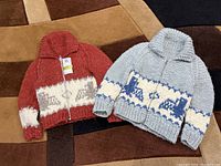 Two knit zip-up cardigans shown side-by-side; one reddish with white and gray animal pattern, one light gray with white and blue animal pattern
