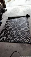 Overhead photo of the black and white diamond patterned outdoor carpet partially rolled at one end, showing overall design and size.