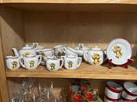 Full set of children's tea dishes on a wooden shelf including teapots, creamers, sugar bowls, plates, cups, saucers, and tureens decorated with Punkinhead character from Eatons.