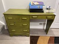 Front view of a solid wood desk painted green with four drawers and visible surface wear. Contents on desk are excluded.