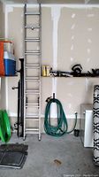 Full view of a 20 foot aluminum extension ladder leaning against a garage wall, showing overall length and condition.