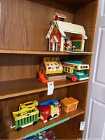 Wide shot showing the Fisher Price school house, cash register, family camper, circus train, picnic basket, and Mattel figures on wooden shelving
