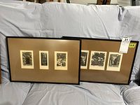 Two black painted wood frames each containing three signed and matted etchings behind glass, placed leaning on couch. Frames show scuff marks and wear.