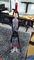 Full view of the Hoover Power Dash carpet cleaner standing upright on a carpet, showing the handle and water tanks.