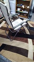 Side view of fabric and steel frame patio lounger on carpeted floor showing fabric sides laced with black cord to frame.