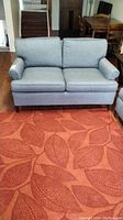 Full front view of gray fabric loveseat with two seat and back cushions, wooden legs, placed on reddish patterned carpet