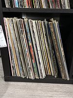 Photo showing approximately 60 LP vinyl records stored vertically on a shelf, old album covers visible on edges.