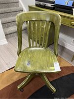 Front view of green wooden office chair showing slatted back and seat with wear spot.