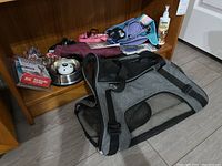 Overall view of pet care items on wooden shelf and floor: soft-sided pet carrier, dog coats, harnesses, water dish, leash, chew toys, pet spray