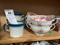 Shows two Wedgwood Blue Pacific cups with cream and blue gradient and four Royal Albert Serena soup dishes with floral patterns stacked behind