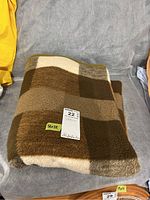Fleece throw blanket folded on a grey surface showing block pattern and size 56x72 inches with identification tags.