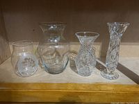Four vases on shelf including two clear glass and two crystal cut vases of various shapes and sizes