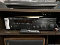 Front view of Yamaha RX-485 stereo receiver with remote on shelf and user manual on top.