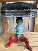 Side view showing the solid wood frame, turned central column painted light blue, cast metal red claw feet, and original black cushion with trim, highlighting the funky paint job and wear.