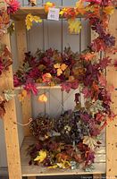 Overview photo of multiple autumn-themed garlands and floral arrangements on wooden shelves showing colorful leaf clusters in red, orange, yellow, and brown.