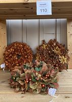 Three autumn/Christmas artificial floral wreaths on a wooden shelf showing full lot and details.