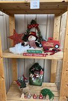 Shelving display with various Christmas decorations including snowman figurine, wreath, star ornament, garland, wooden signs, greenery arrangement, and reindeer headbands.